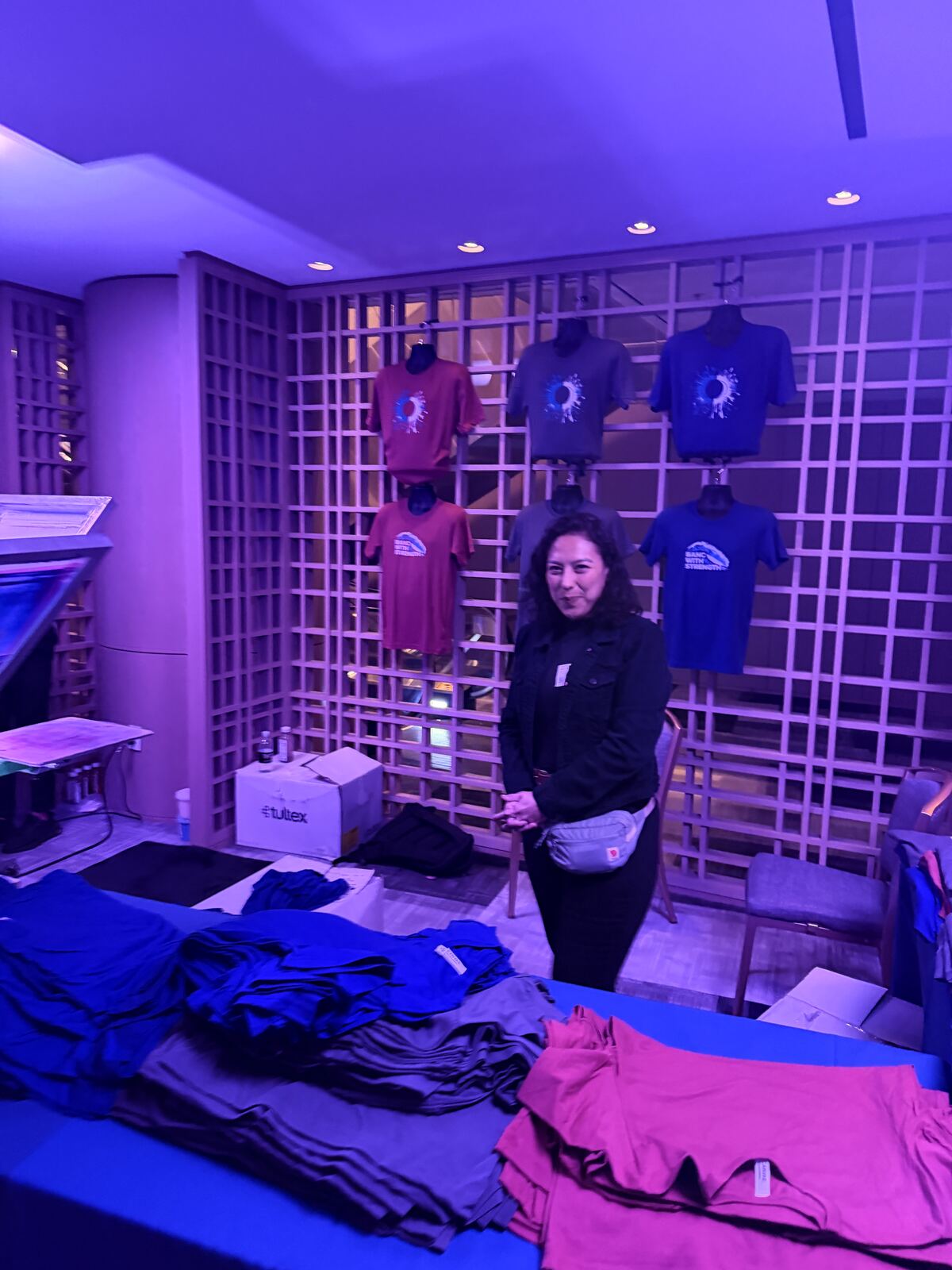 Guest interacting with screen-printed apparel samples on a blue booth table at an indoor event