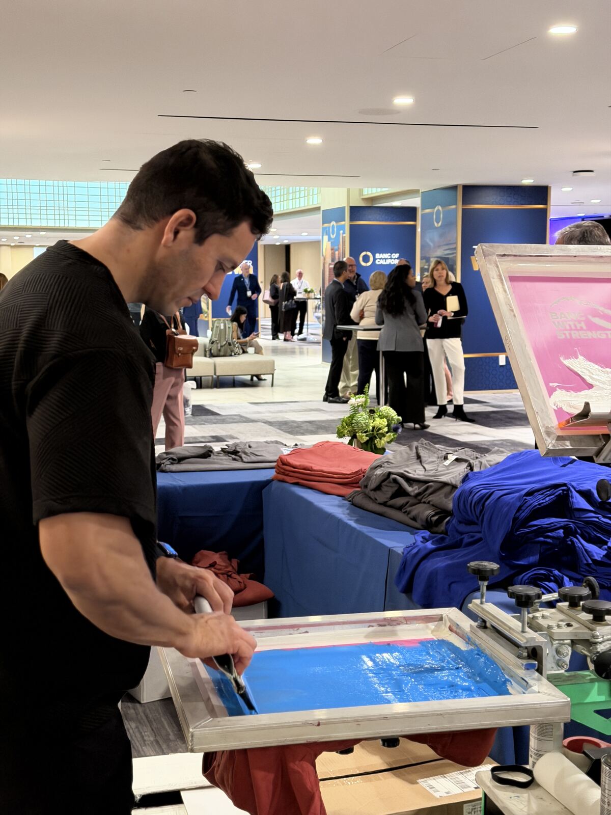 Staff demonstrating screen printing equipment with red screens and blue t-shirts displayed at a booth
