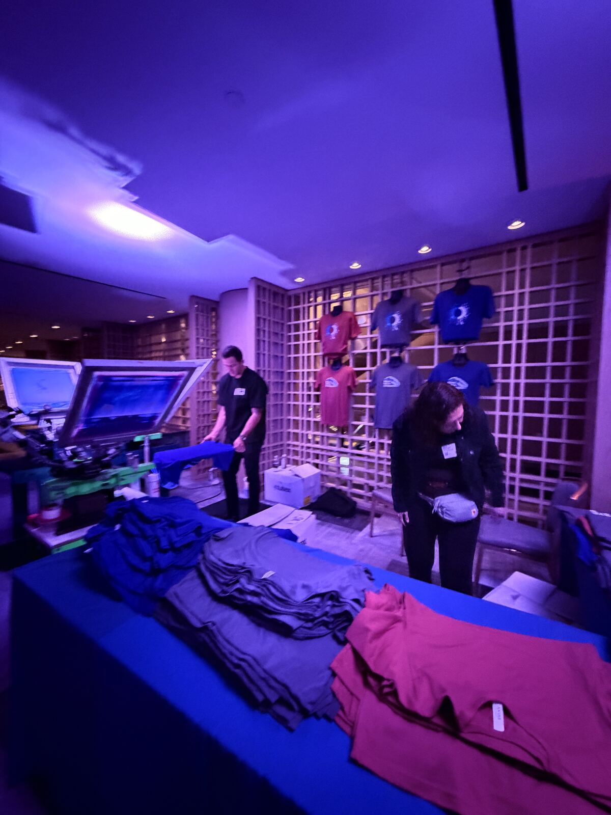 Staff member displaying a heat-pressed apparel sample with vibrant neon text at an event booth